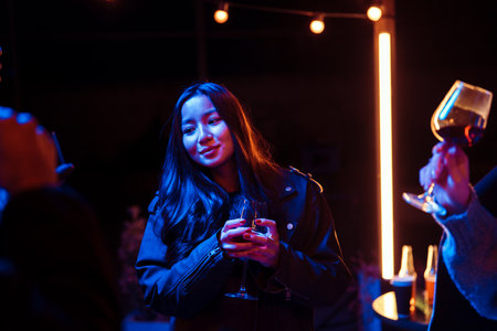 Friends celebrate at night gathering with drinks and vibrant lights in an outdoor settingの写真素材