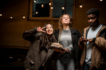 Friends celebrating with a cake in a cozy, dimly lit setting during an evening gatheringの写真素材
