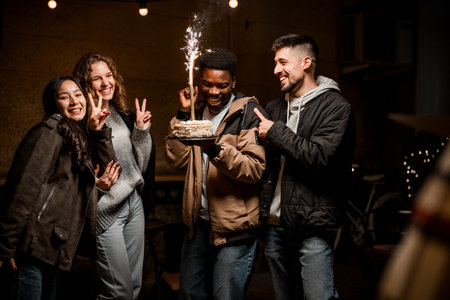 Friends celebrating with a cake and sparkler at a cozy indoor gathering during an evening eventの写真素材