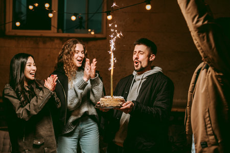 Friends celebrating a birthday with a cake and fireworks indoors at night