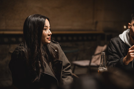 Friends enjoying an evening conversation in a cozy indoor setting with warm lightingの写真素材