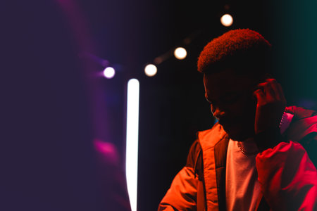 Young man focused on DJ equipment in a vibrant nightclub setting during an evening event