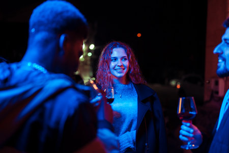 Friends enjoying wine together at a lively night gathering under colorful lights