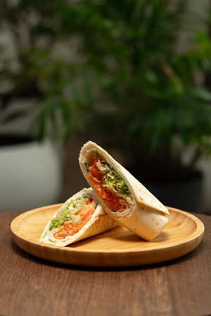 Freshly wrapped salad wraps served on a wooden plate with green plants in the backgroundの写真素材