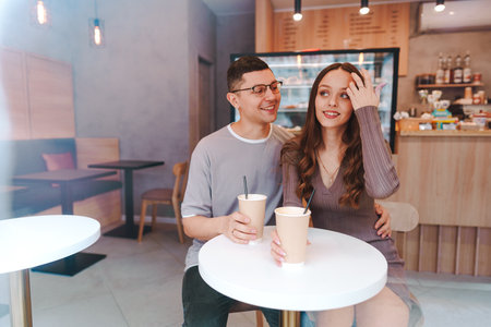 Young couple enjoying coffee together in a modern cafe during the day, sharing smiles and laughterの写真素材