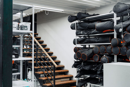 Storage area showing neatly organized black gear bags on shelves with wooden stairs in a well-lit spaceの写真素材