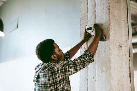 Skilled worker installing security camera on concrete pillar in modern workspace in the afternoon