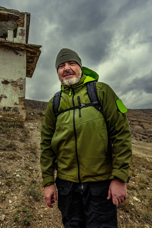 Hiker stands confidently near an abandoned building against a dramatic cloudy sky in a mountainous regionの写真素材