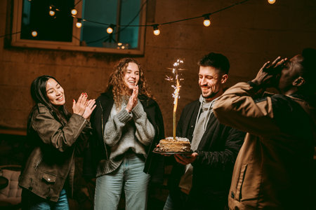 Celebration with friends and a sparkling cake during nighttime gathering in cozy atmosphereの写真素材