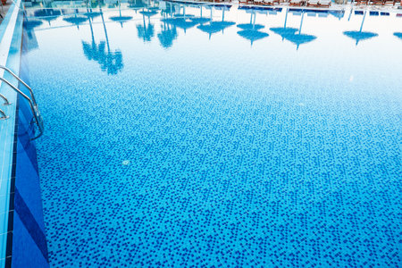 Bright blue swimming pool reflecting palm trees in sunny outdoor settingの写真素材