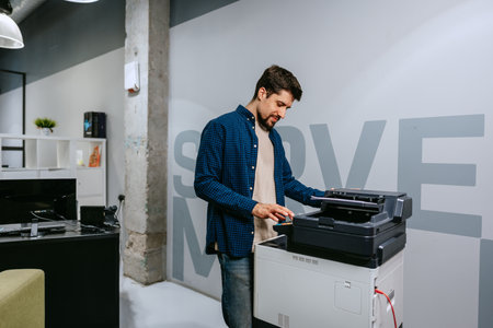 Man operates a printer in a modern office environment during daylight, focused on completing tasks...