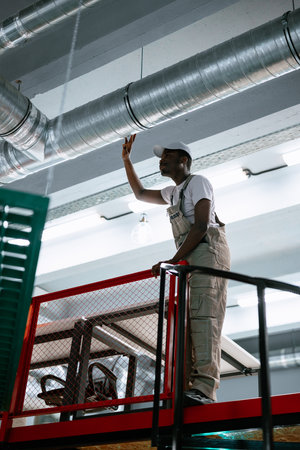 Worker on elevated platform adjusting air duct in commercial building during daytimeの写真素材