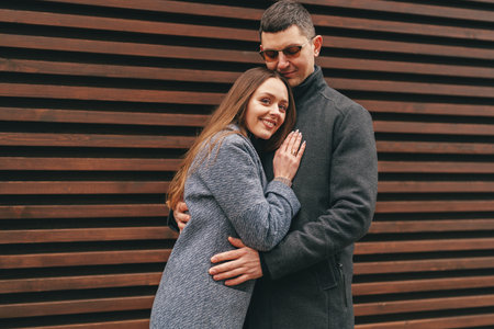 Couple embraces affectionately while posing against a wooden wall in a cozy urban setting during autumnの写真素材