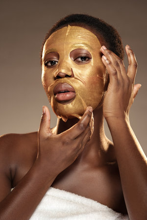 Woman applying a luxurious gold facial mask at a spa during a self-care sessionの写真素材