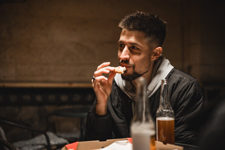 Man enjoying food and drink in a cozy setting during the evening with friends nearbyの写真素材
