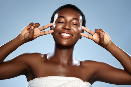 Woman smiles and poses cheerfully with peace signs against a light blue background in a studio settingの写真素材