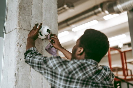 Worker cleans surveillance camera in an industrial setting during daylight hoursの写真素材