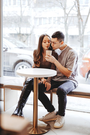 Couple enjoys warm drinks together in a cozy cafe while winter snow falls outsideの写真素材
