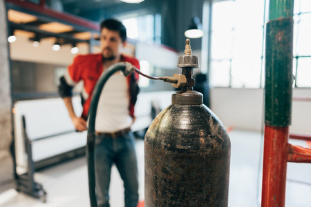Worker inspecting a gas cylinder in a modern workspace during daylight hoursの写真素材