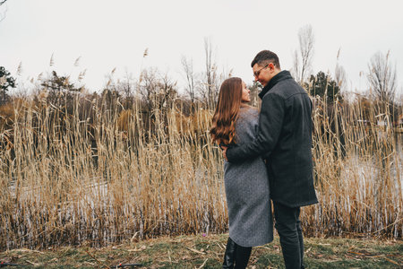 Couple enjoys a romantic moment by a serene waterway during autumn in a park during cool weatherの写真素材