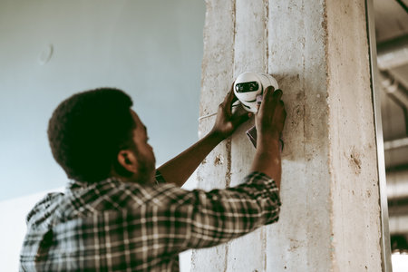 Technician installing security camera in modern office space during daylight hoursの写真素材