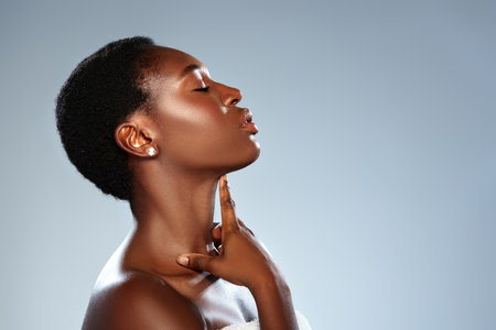 Elegant woman showcases beauty with poised expression and gentle hand on her neck against a soft blue backgroundの写真素材