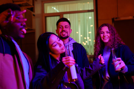 Friends enjoying a lively gathering indoors at night with colorful lights and drinks in handの写真素材