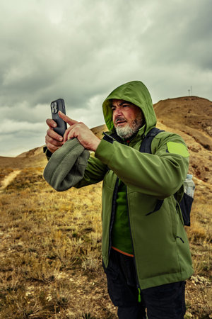 Man takes a photo with smartphone while hiking in rugged landscape under cloudy sky