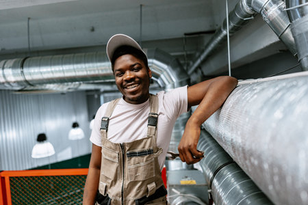 Skilled worker smiles proudly while standing on a platform in a well-lit industrial workspace during the dayの写真素材