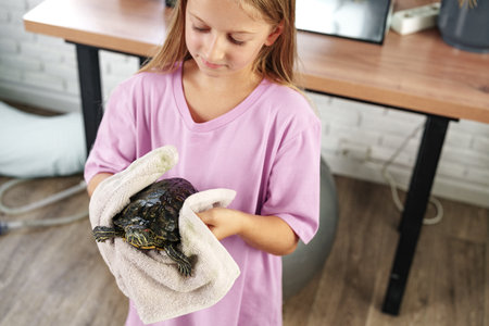 Young girl carefully holds a turtle wrapped in a towel in a cozy indoor space during the dayの写真素材