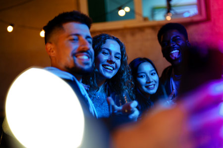 Friends enjoying a vibrant outdoor gathering at night with colorful lights and drinks in hand