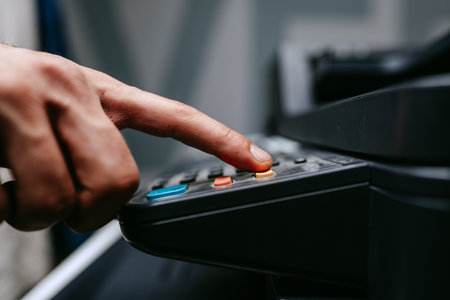 Person pressing buttons on office equipment in a busy workspace during the dayの写真素材