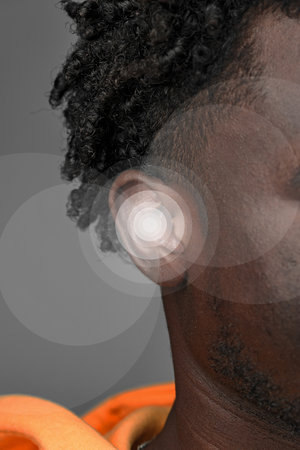 Detailed close-up of a person wearing an orange garment while showcasing an innovative hearing technology on a gray backdropの写真素材