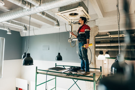 Worker installs HVAC unit in modern building interior during daytime renovation projectの写真素材