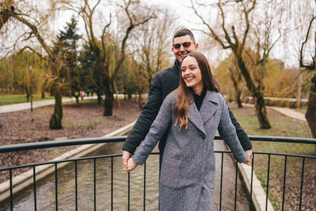 Couple enjoys a joyful moment together on a bridge in a park surrounded by trees in early springの写真素材