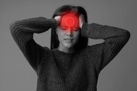 Young woman experiencing severe headache in a minimalistic indoor setting during daylight hoursの写真素材