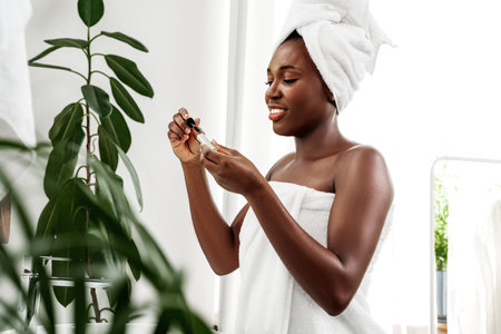 Woman applying skincare serum in a bright bathroom with plants during a self-care routineの写真素材