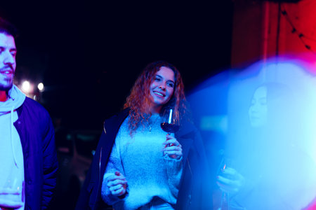 Friends enjoying a night out at an outdoor gathering with colorful lights and drinks in hand