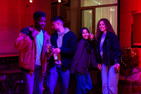Friends enjoying a lively evening at a cozy venue with colorful lighting and drinks in handの写真素材