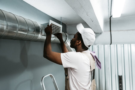 Worker repairs air vent in a commercial building during mid-morning hours of a busy weekdayの写真素材