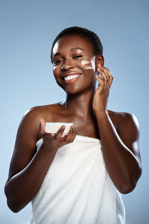 Woman applying skincare product with a joyful expression in a bright settingの写真素材