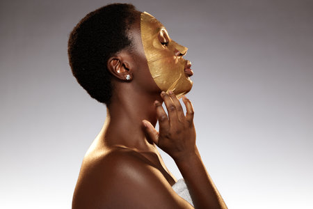 Woman applying gold facial mask in spa setting during a self-care ritual for rejuvenation and relaxationの写真素材