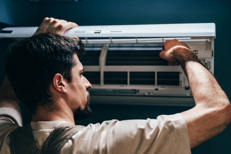 Technician performs maintenance on wall-mounted air conditioning unit in a modern roomの写真素材