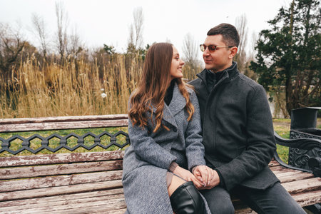 Couple enjoying a quiet moment on a park bench during a chilly afternoon in late fallの写真素材