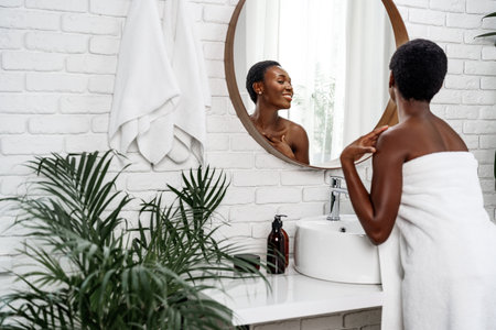 Woman smiles at her reflection in a stylish bathroom while preparing for her day in a serene environmentの写真素材