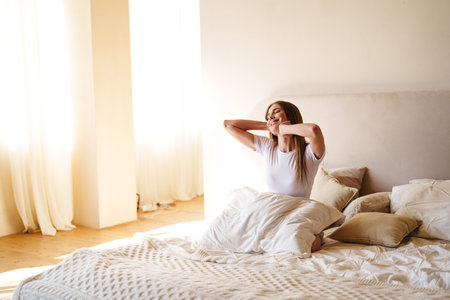 Morning routine in a bright bedroom with a woman stretching and enjoying the sunlightの写真素材