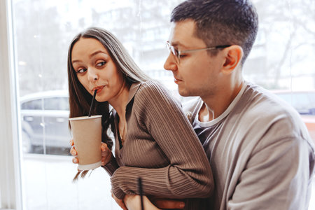 Couple enjoying drinks indoors while sharing a playful moment in a cozy cafe setting on a winter dayの写真素材