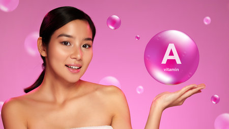 Woman holding vitamin A bubble on her palm against a pink background while promoting skin health and beautyの写真素材