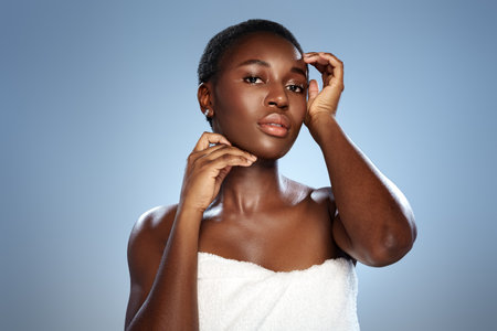 Model posing elegantly against a soft blue backdrop while wearing a towel, showcasing natural beauty and confidence in a studio settingの写真素材