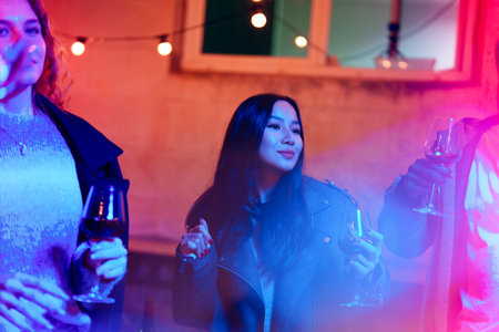 People enjoying a vibrant evening gathering with drinks and colorful lights in an outdoor settingの写真素材